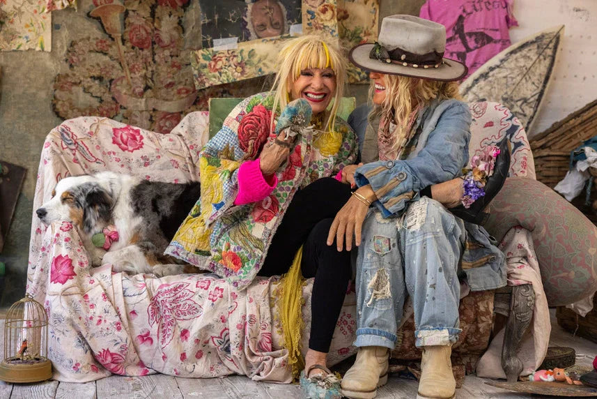 Two women in Magnolia Pearl artisan vintage clothing on floral couch, whimsical decor, dog beside them