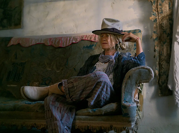 Woman in Magnolia Pearl artisan clothing with whimsical, vintage style sitting on rustic sofa