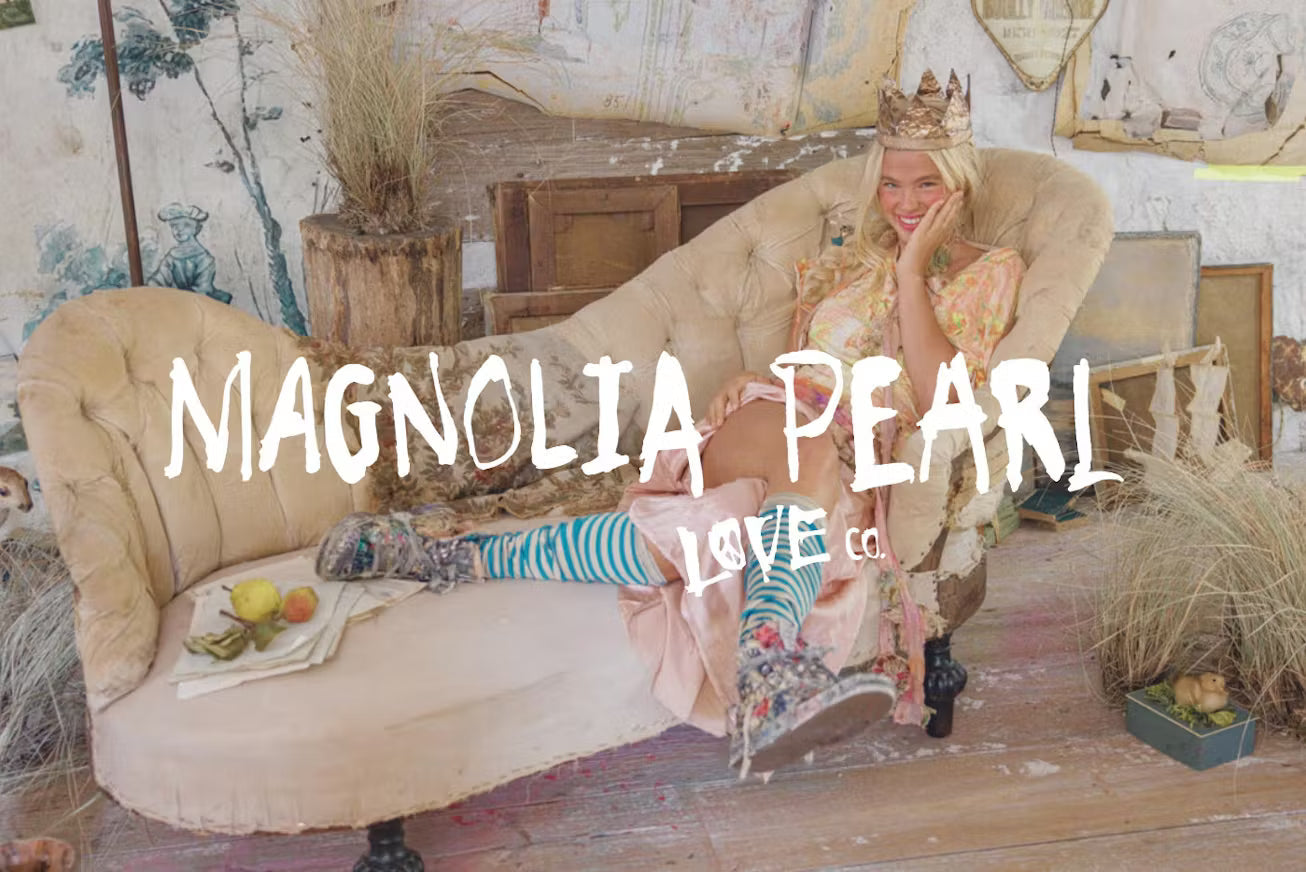 Woman in whimsical Magnolia Pearl vintage artisan clothing, crown, striped socks, lounging on antique sofa in eclectic rustic setting
