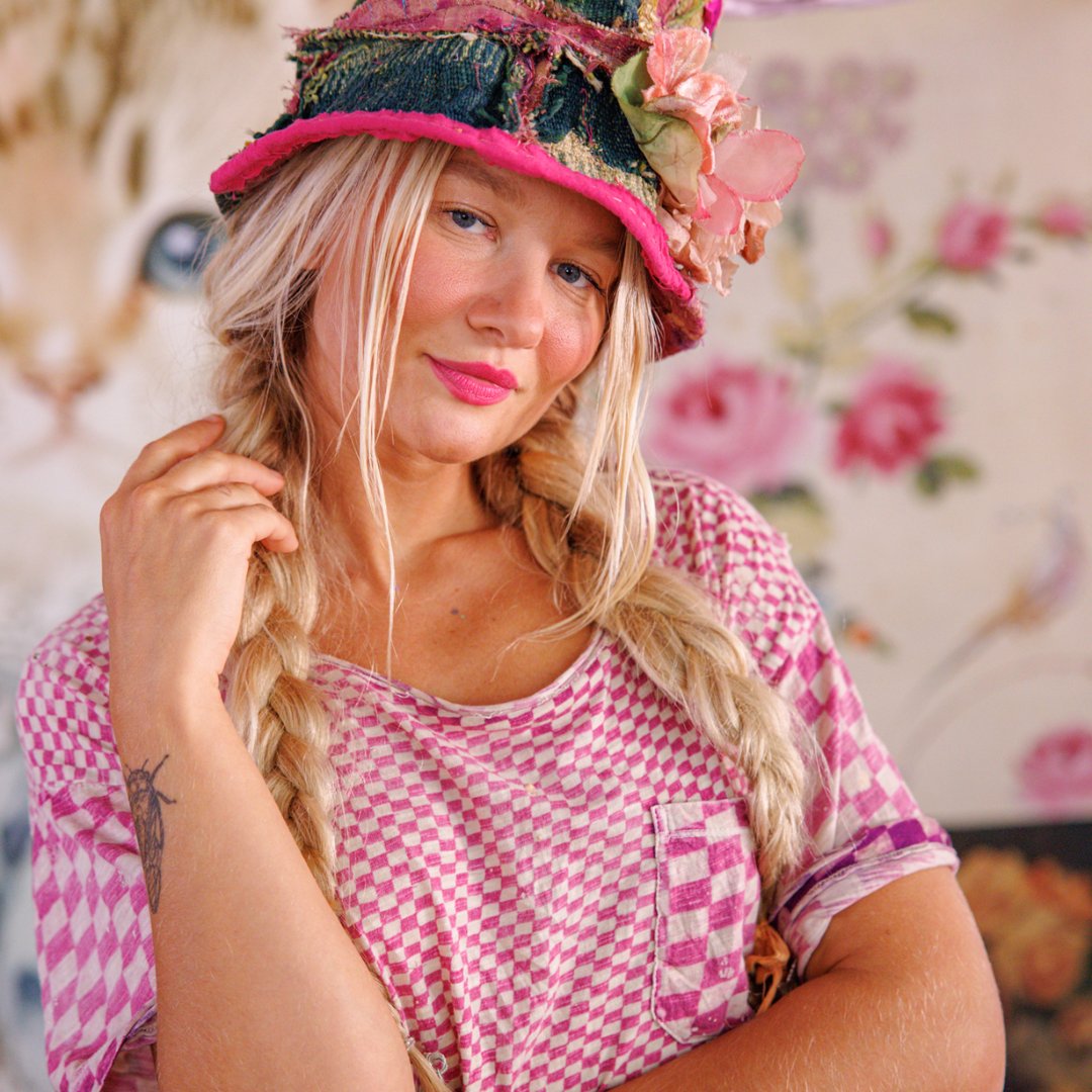Woman in Magnolia Pearl artisan checkered pink shirt and whimsical floral hat, vintage style
