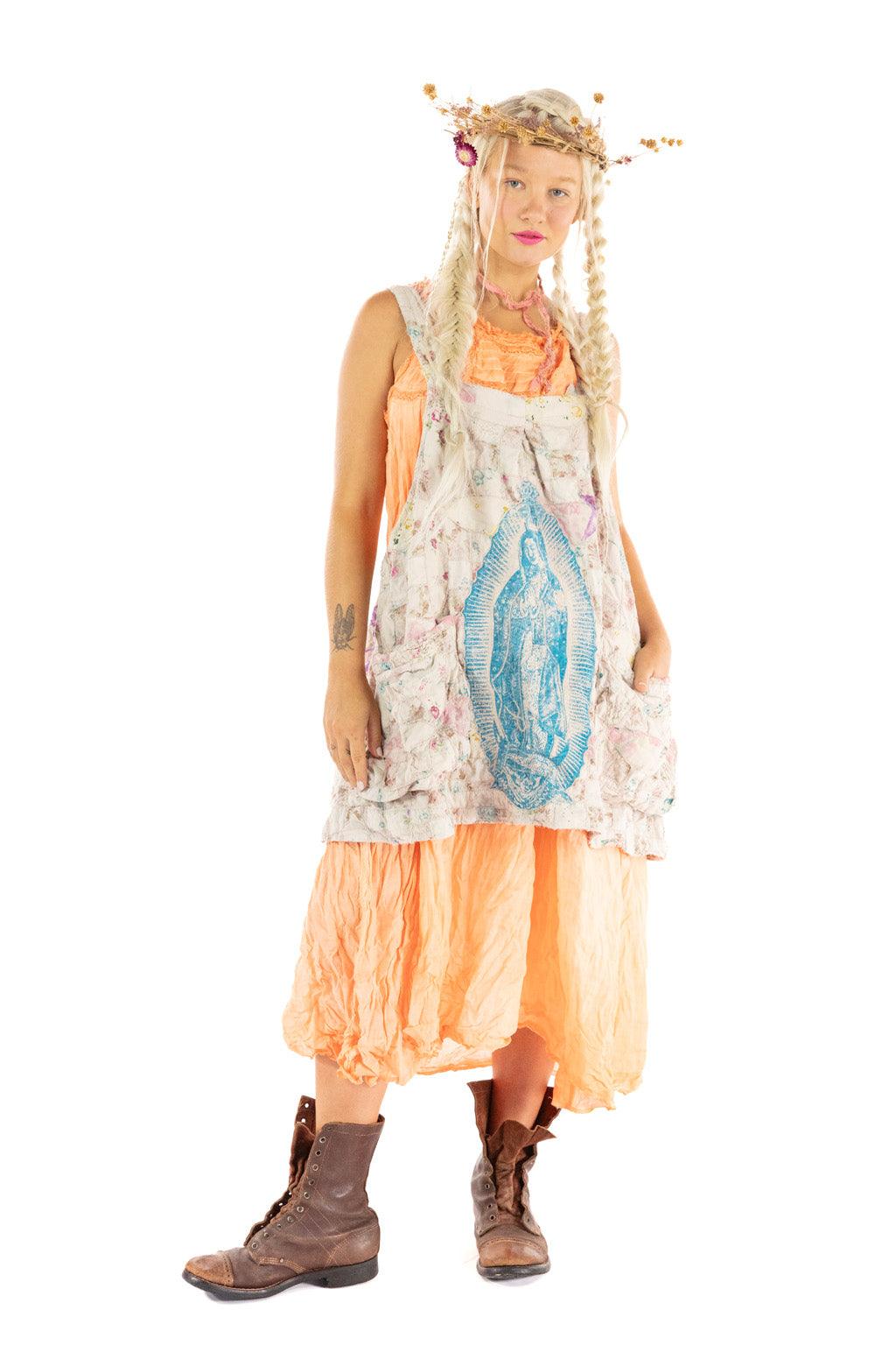Woman in Magnolia Pearl whimsical artisan apron dress with vintage floral pattern and Virgin Mary print, styled with boots and flower crown