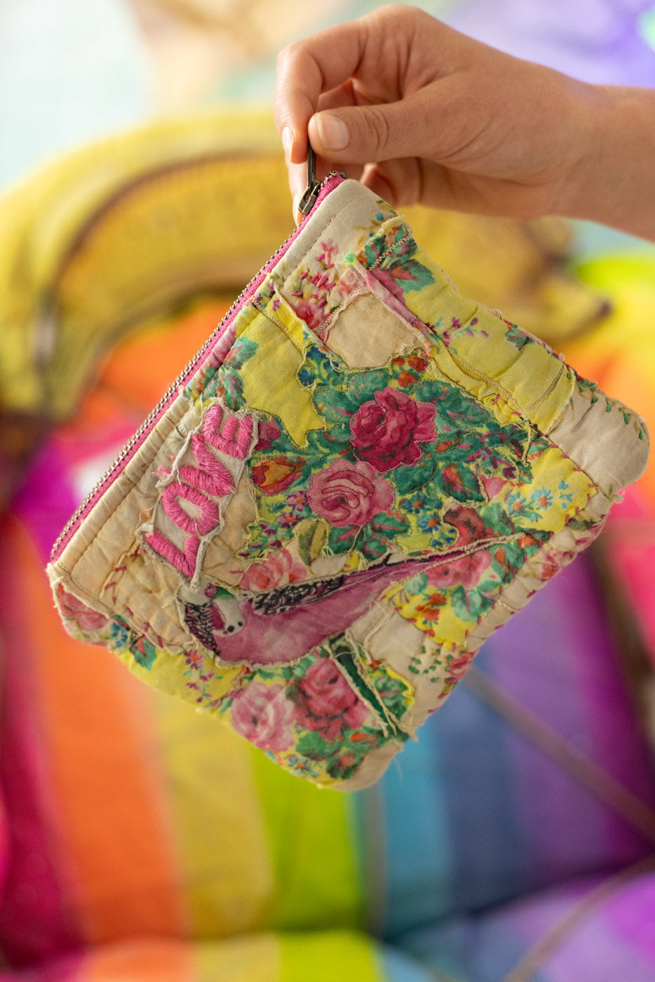 Floral-patterned patchwork pouch / make-up bag / held by a hand with colorful background
