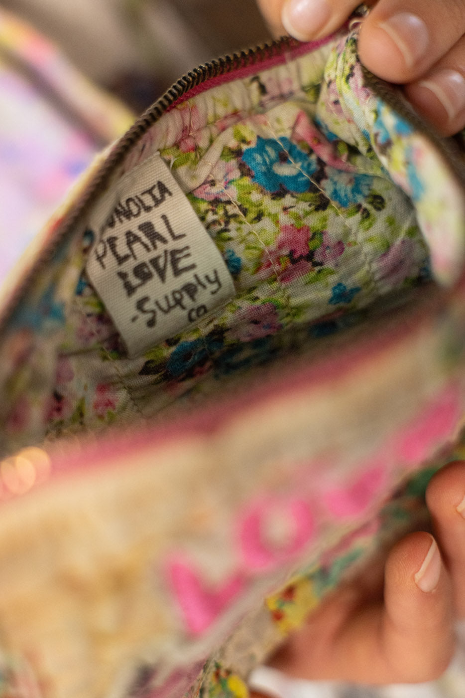 Floral-patterned zipper pouch / makeup bag  / small bag with a magnolia pearl love supply co. label inside, held by hands.