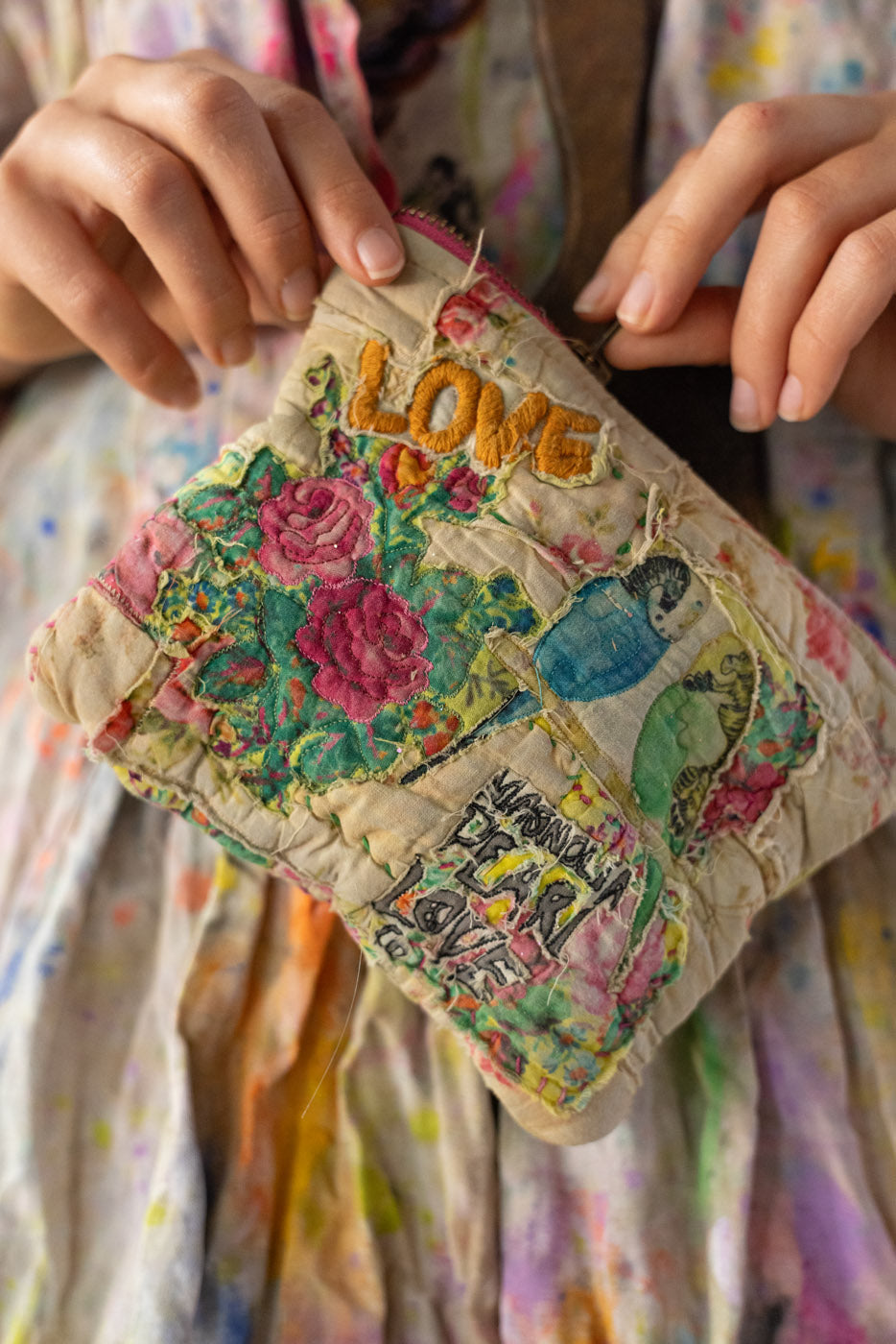 Handmade patch with floral designs on a zipper bag / pouch /  and 'LOVE' text held by a person wearing a colorful dress.