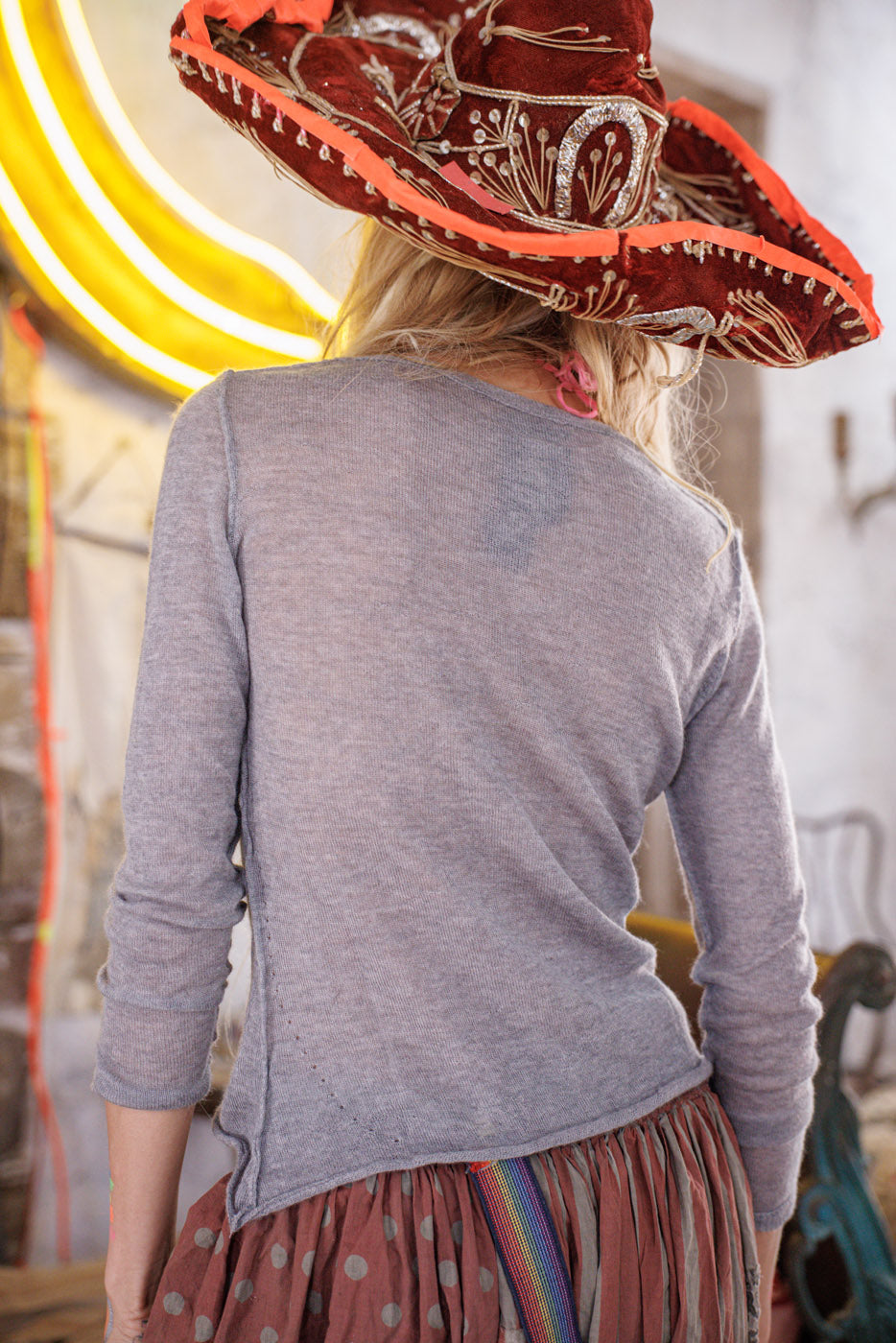 Back view of woman in whimsical Magnolia Pearl artisan gray cashmere top, vintage polka dot skirt, and red embroidered hat
