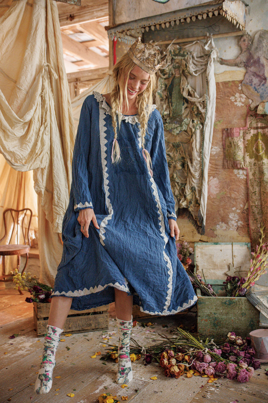 Woman in vintage blue Magnolia Pearl dress with whimsical socks and paper crown, floral artisan setting