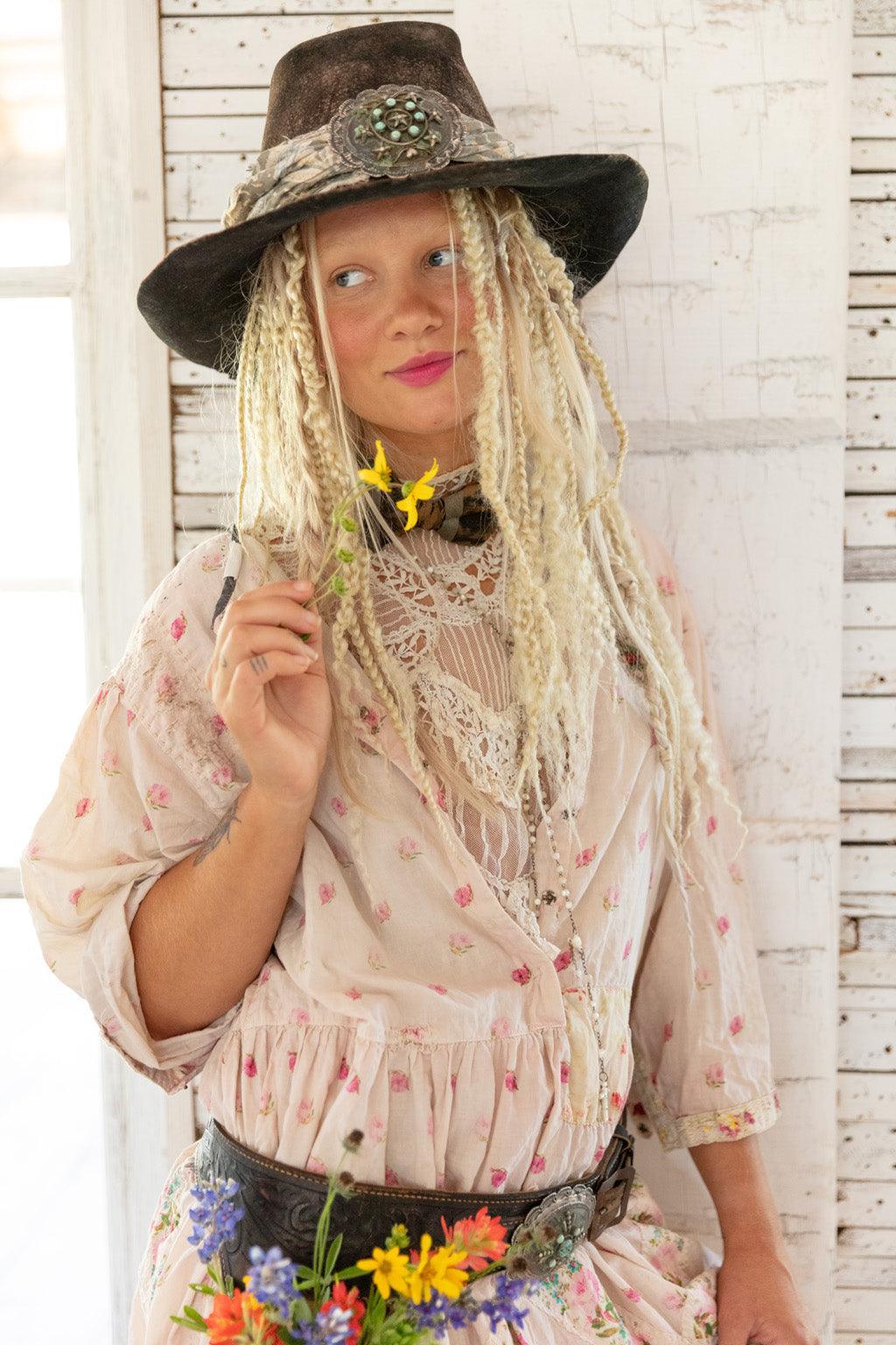 Woman in Magnolia Pearl vintage floral dress and artisan hat holding yellow wildflower