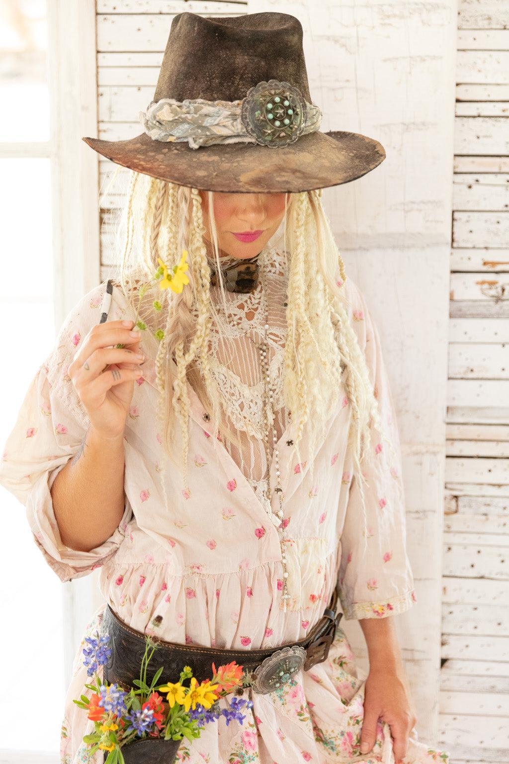 Woman in Magnolia Pearl artisan floral dress and vintage hat, holding wildflowers, whimsical style
