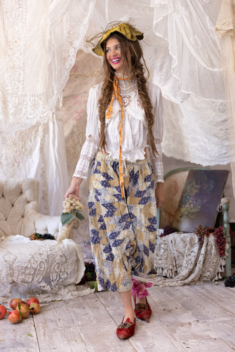 Magnolia Pearl model in vintage artisan clothing, whimsical lace setting, holding grapes, artful decor