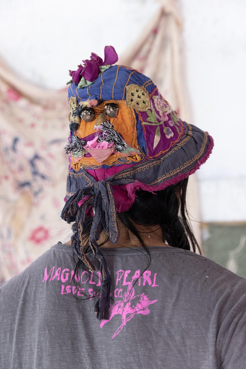 Magnolia Pearl artisan patchwork bucket hat with vintage whimsical floral details, worn by smiling model in gray LOVE shirt