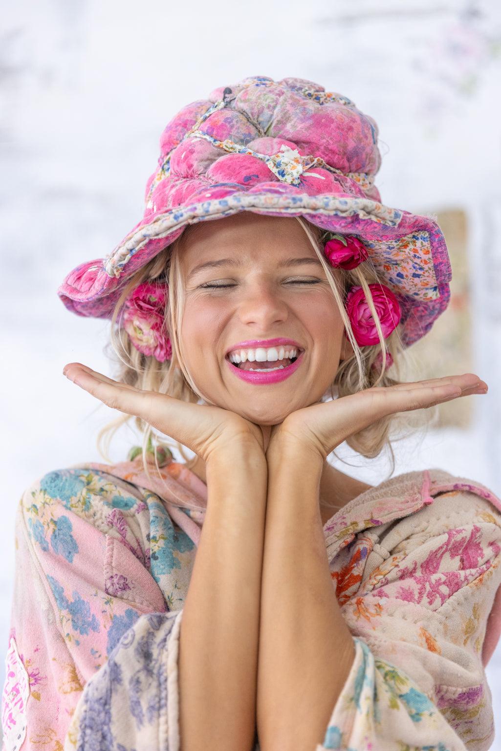 Smiling woman in whimsical Magnolia Pearl pink floral patchwork hat and vintage quilted jacket