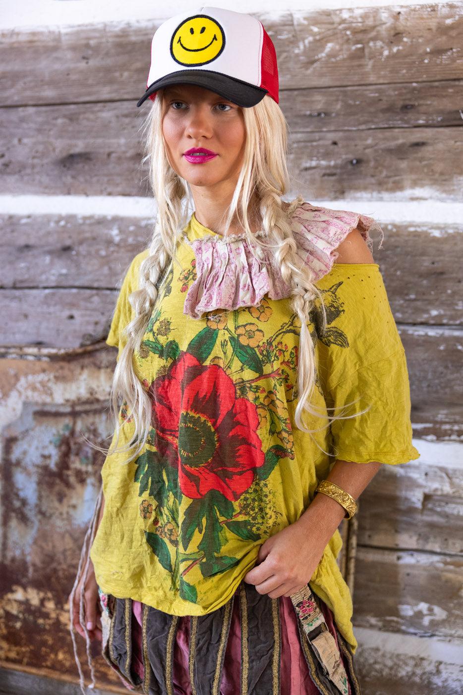 Woman in Magnolia Pearl yellow artisan top with floral print, ruffled collar, and smiley hat