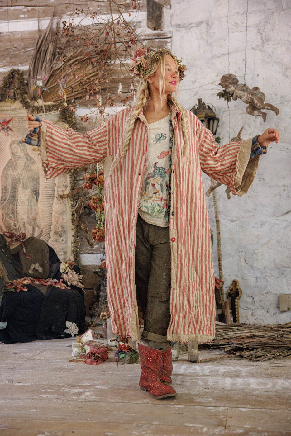 Woman in Magnolia Pearl artisan striped vintage coat, floral crown, and glitter boots, rustic setting