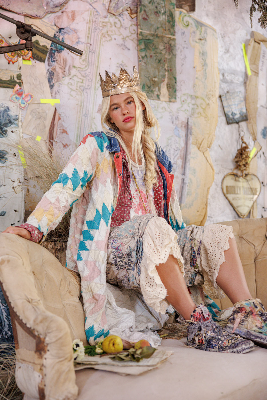 Woman in patchwork jacket and crown sitting on vintage sofa in eclectic, artistic room