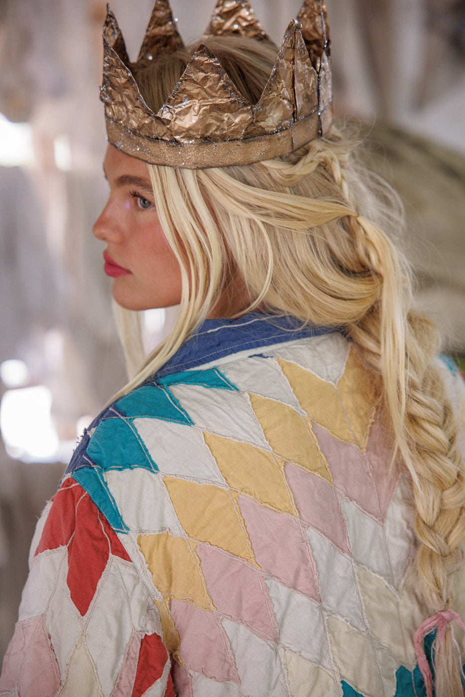 Woman in crown and patchwork jacket with pastel diamond pattern, blonde hair in braid