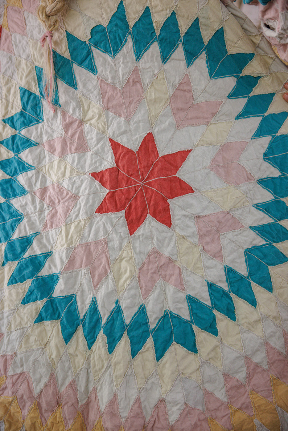 Colorful handmade quilt with geometric starburst pattern in red, pink, teal, and cream fabrics