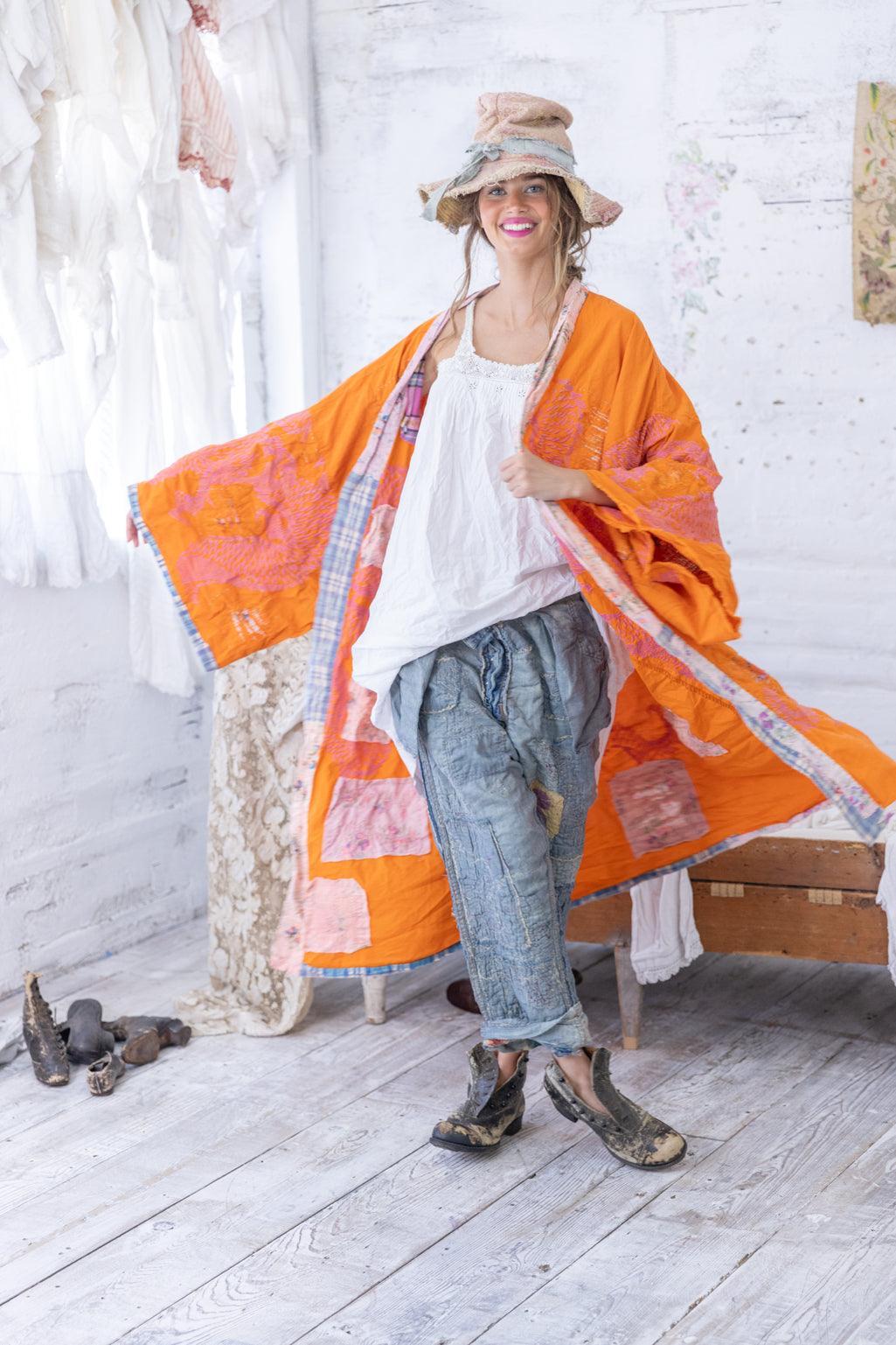 Woman in Magnolia Pearl artisan orange patchwork kimono, vintage jeans, whimsical hat, rustic studio