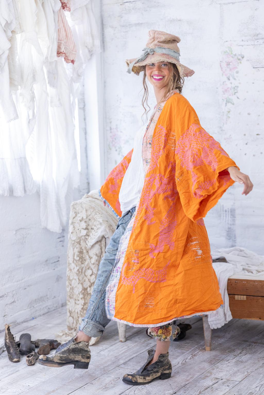 Woman in Magnolia Pearl artisan orange patchwork kimono, vintage jeans, whimsical hat, rustic studio