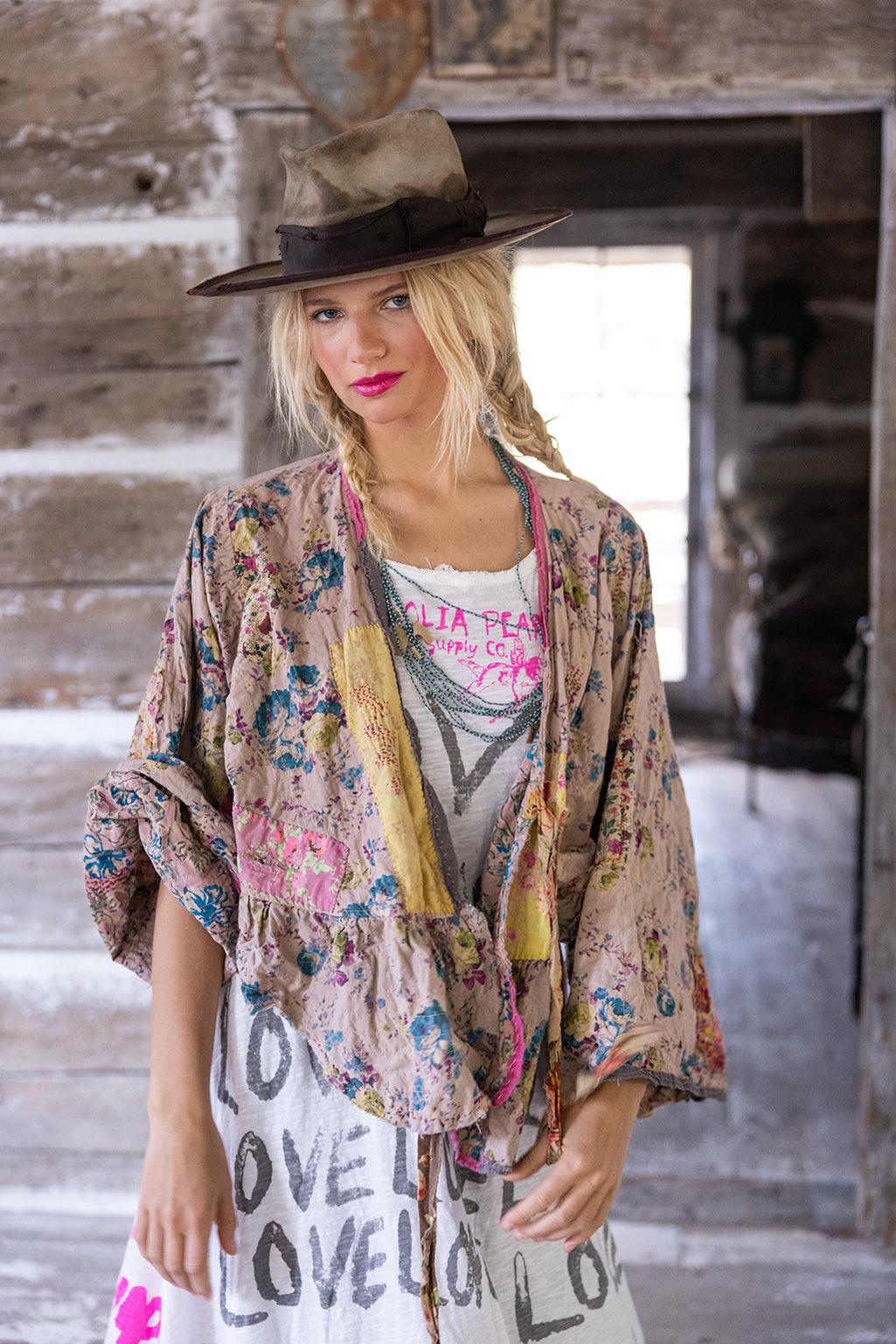 Woman in Magnolia Pearl vintage artisan dress with LOVE print, floral jacket, and hat in rustic setting
