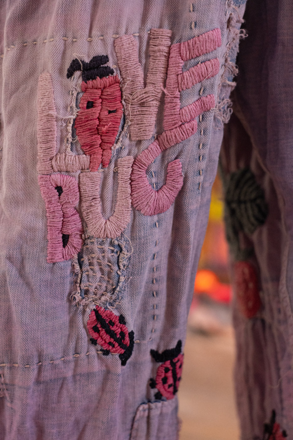Embroidered design on the of purple denim overalls with pink and black elements.