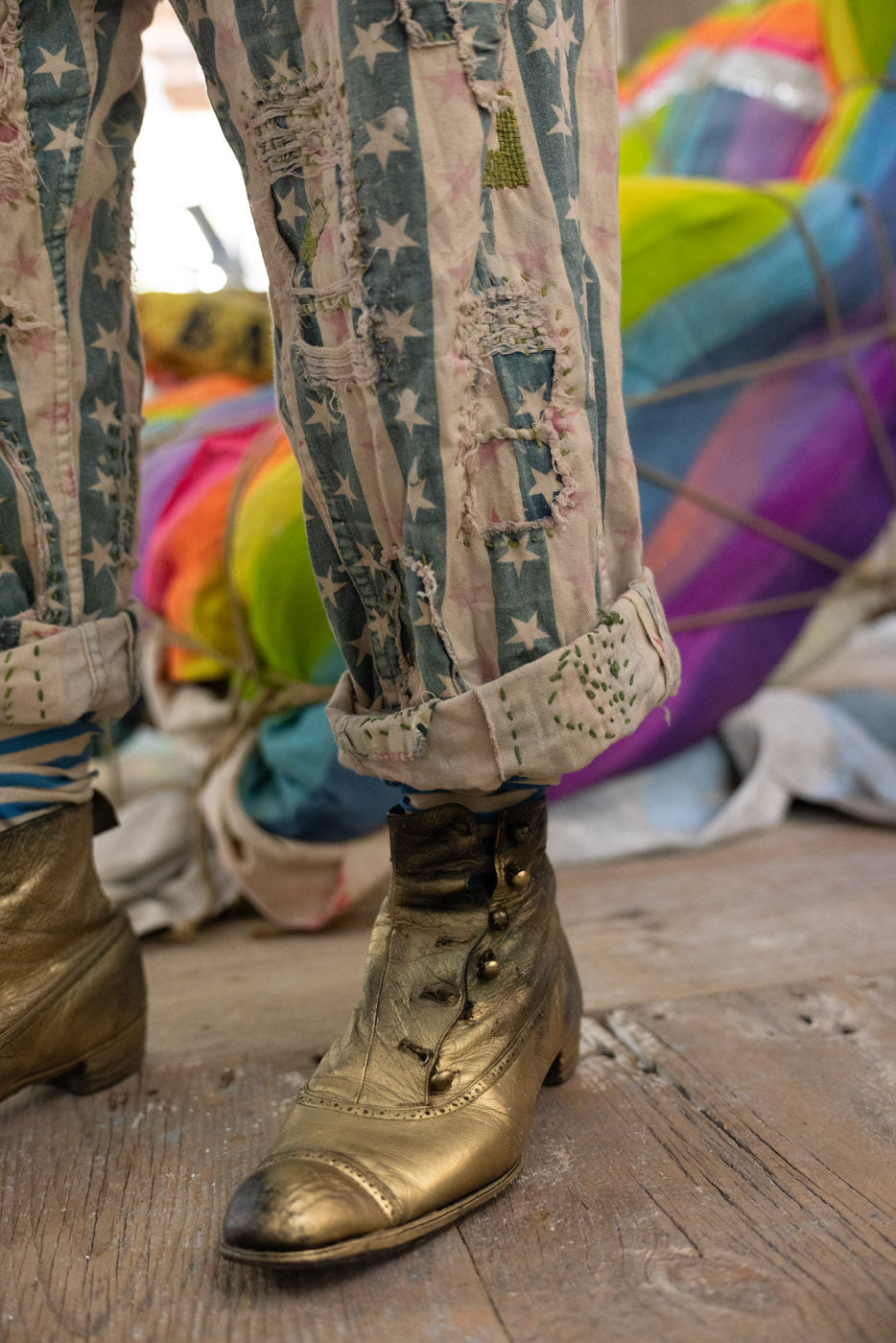 Person wearing gold boots and patterned pants with a colorful background