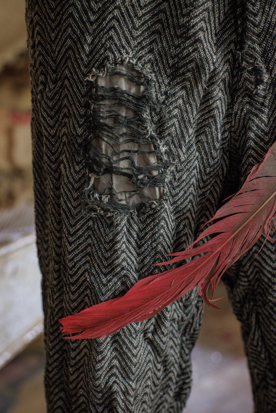 Distressed herringbone pants with ripped patch and red feather accent