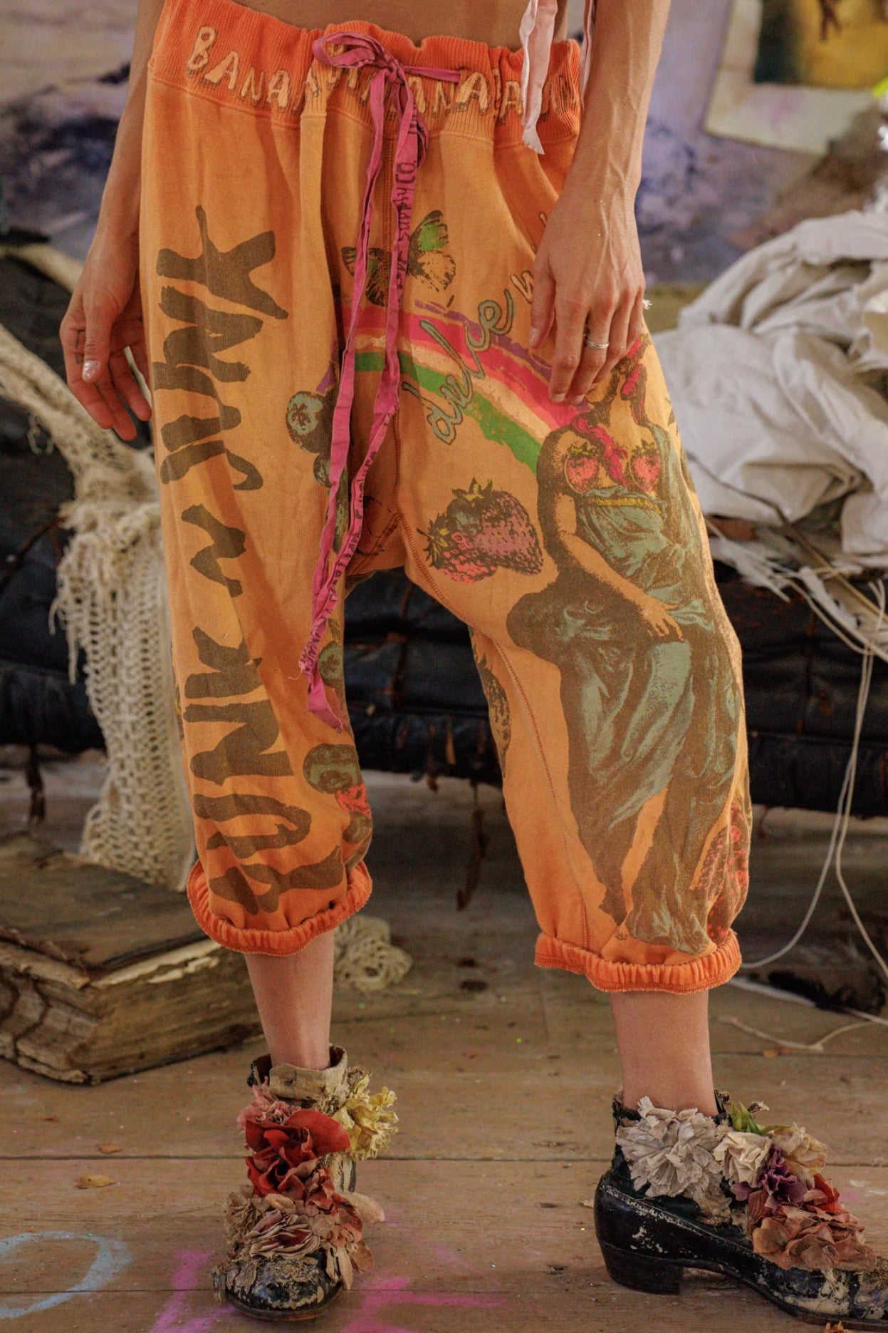 Person wearing orange sweats with graphic designs in a rustic indoor setting.