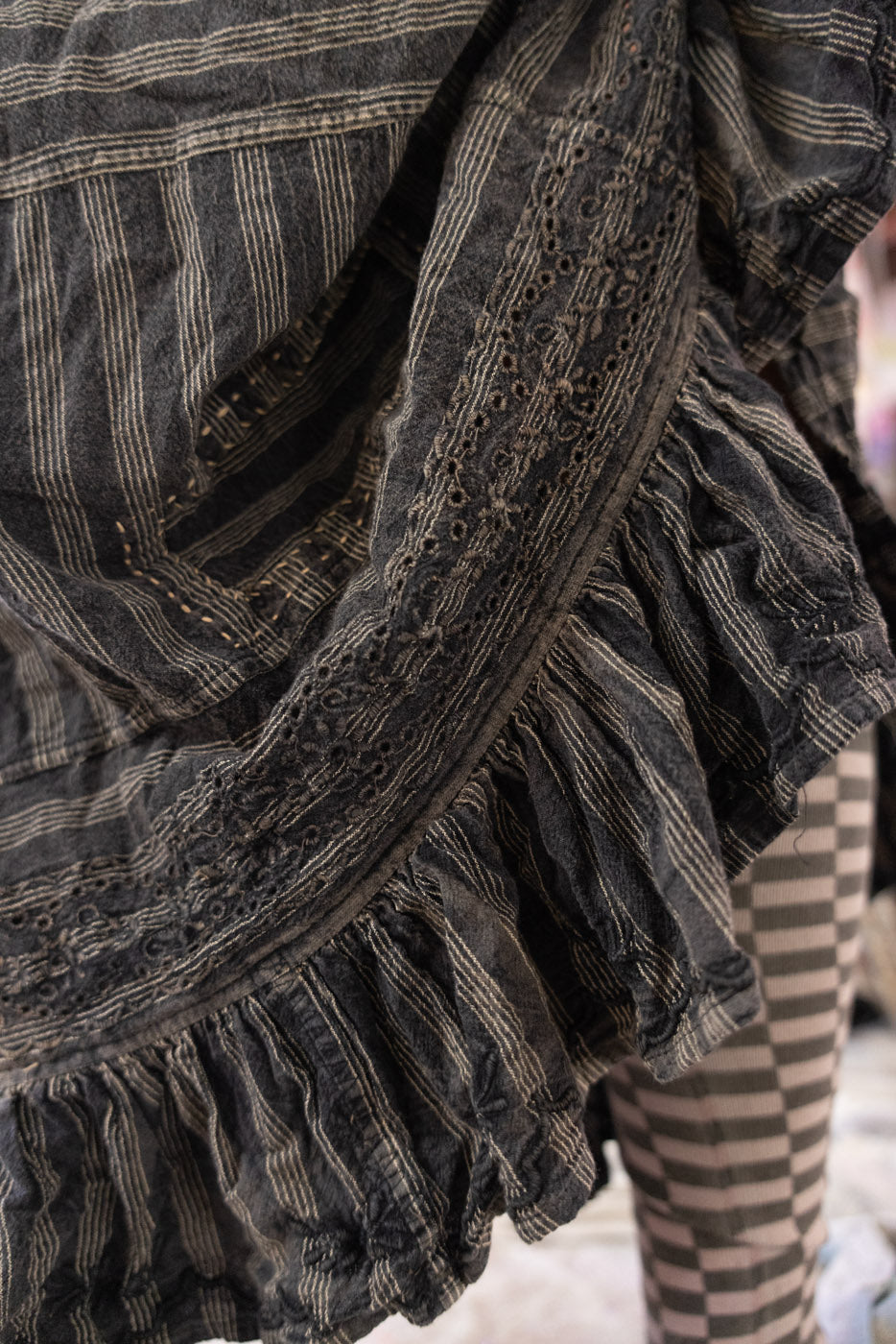 Close-up of a textured gray skirt with ruffled edges and striped pattern socks in the background