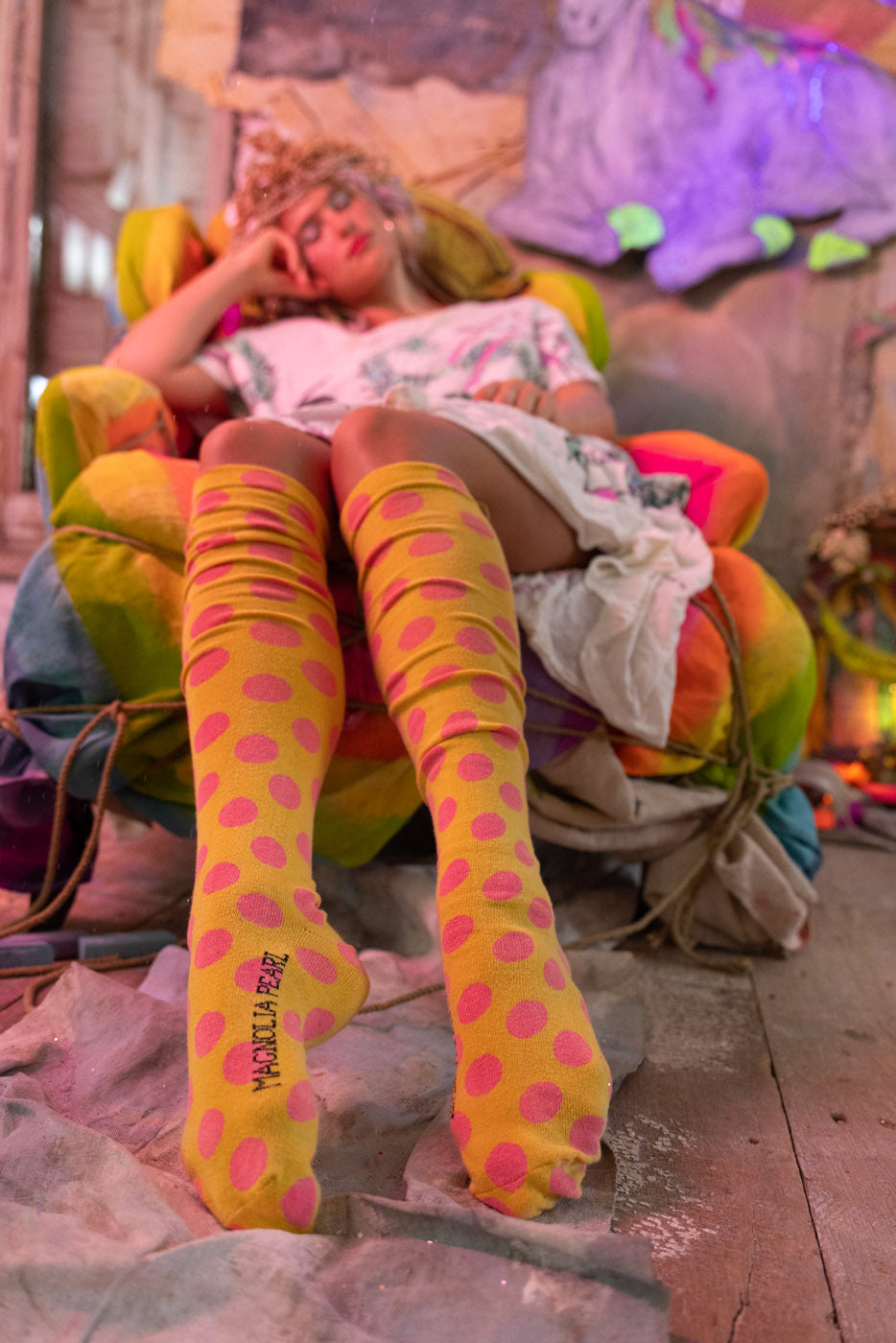 Person wearing bright yellow and pink polka dot socks sitting on a colorful chair with a blurred background
