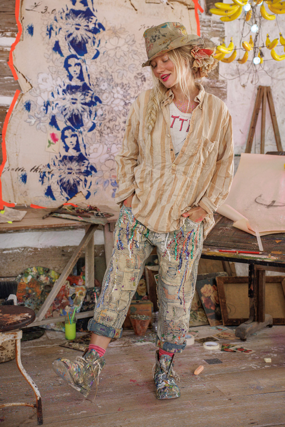 Woman in Magnolia Pearl artisan clothing with whimsical, vintage patched pants and striped shirt in colorful, creative studio