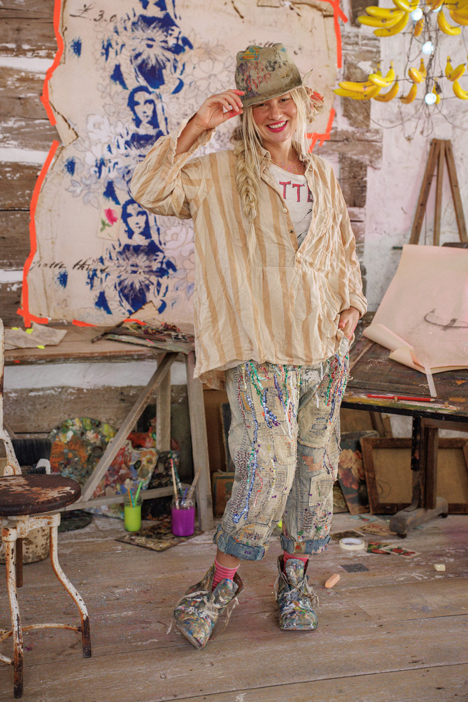 Woman in Magnolia Pearl artisan clothing with whimsical, vintage patched pants and striped shirt in colorful, creative studio