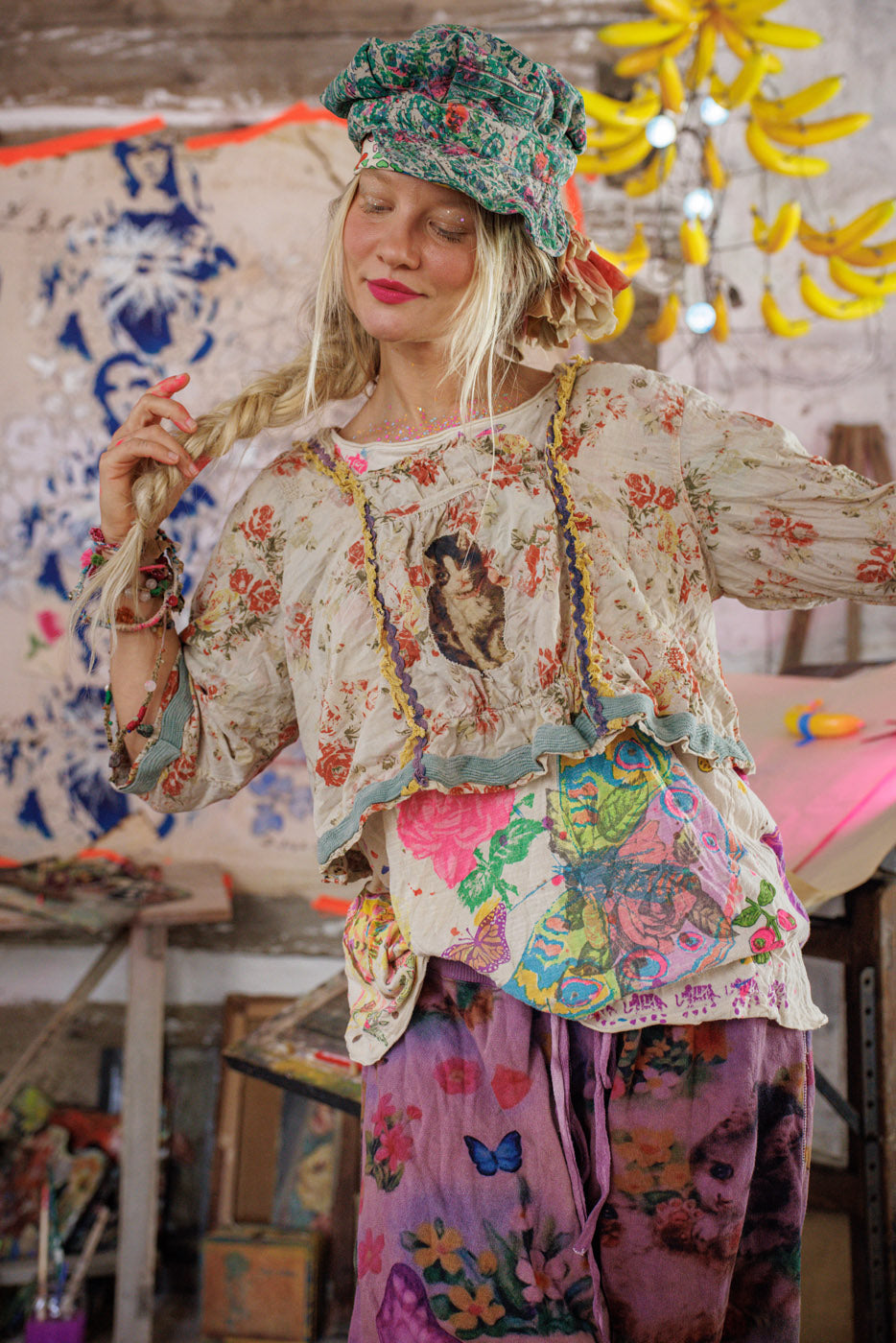 Woman in Magnolia Pearl artisan floral vintage top, colorful pants, and whimsical green hat