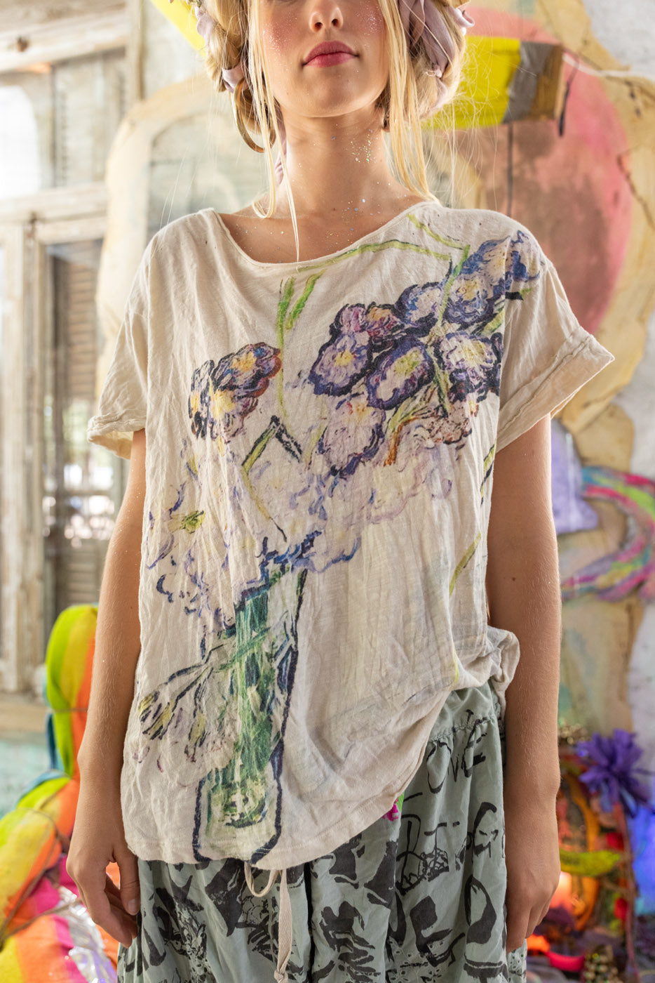 Person wearing a floral-patterned  Magnolia Pearl shirt with a colorful, abstract background