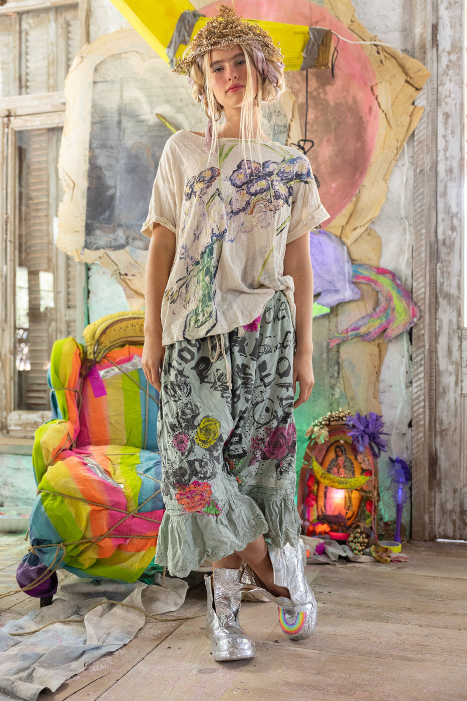 Person wearing a colorful outfit in a vibrant, artistic setting with a rainbow chair and abstract art.