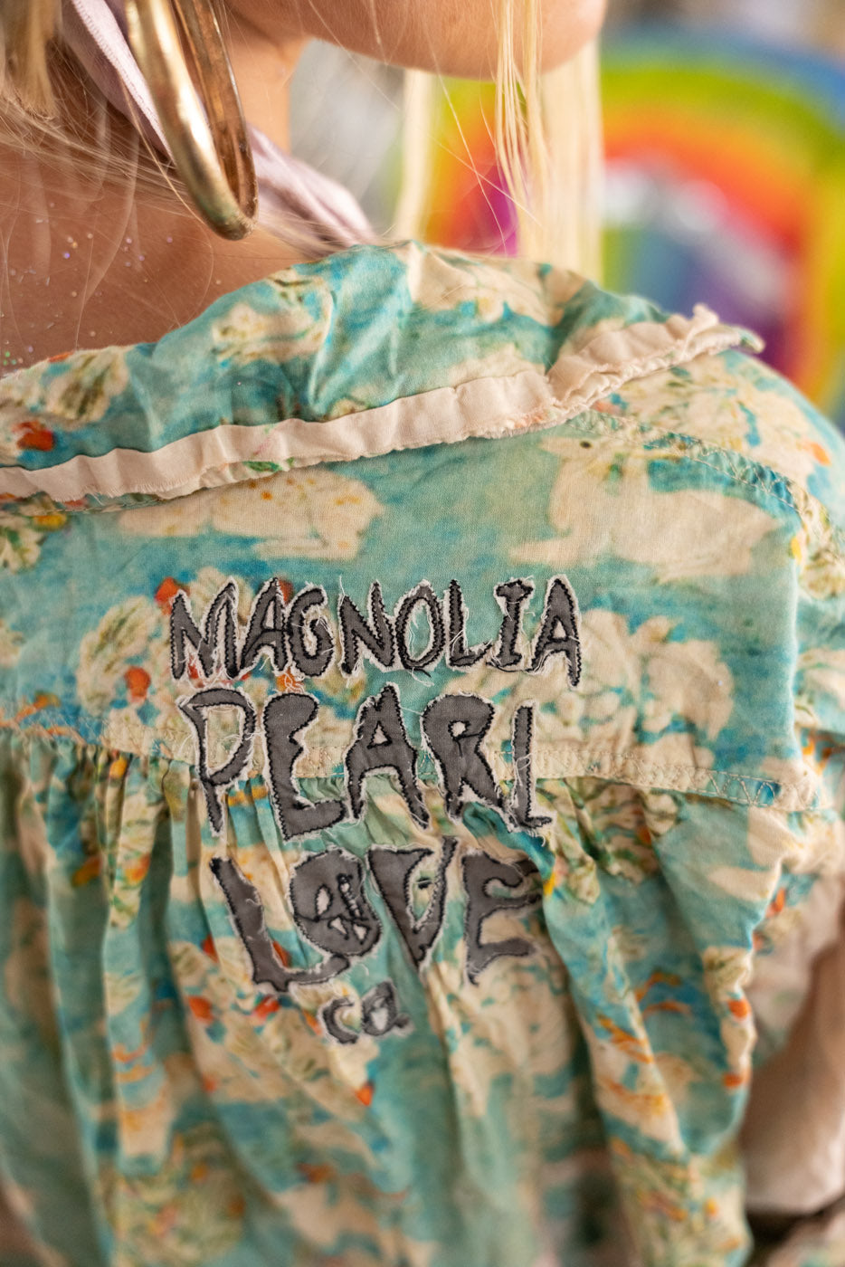 Back view of a floral-patterned blouse with 'Magnolia Pearl Love' branding.