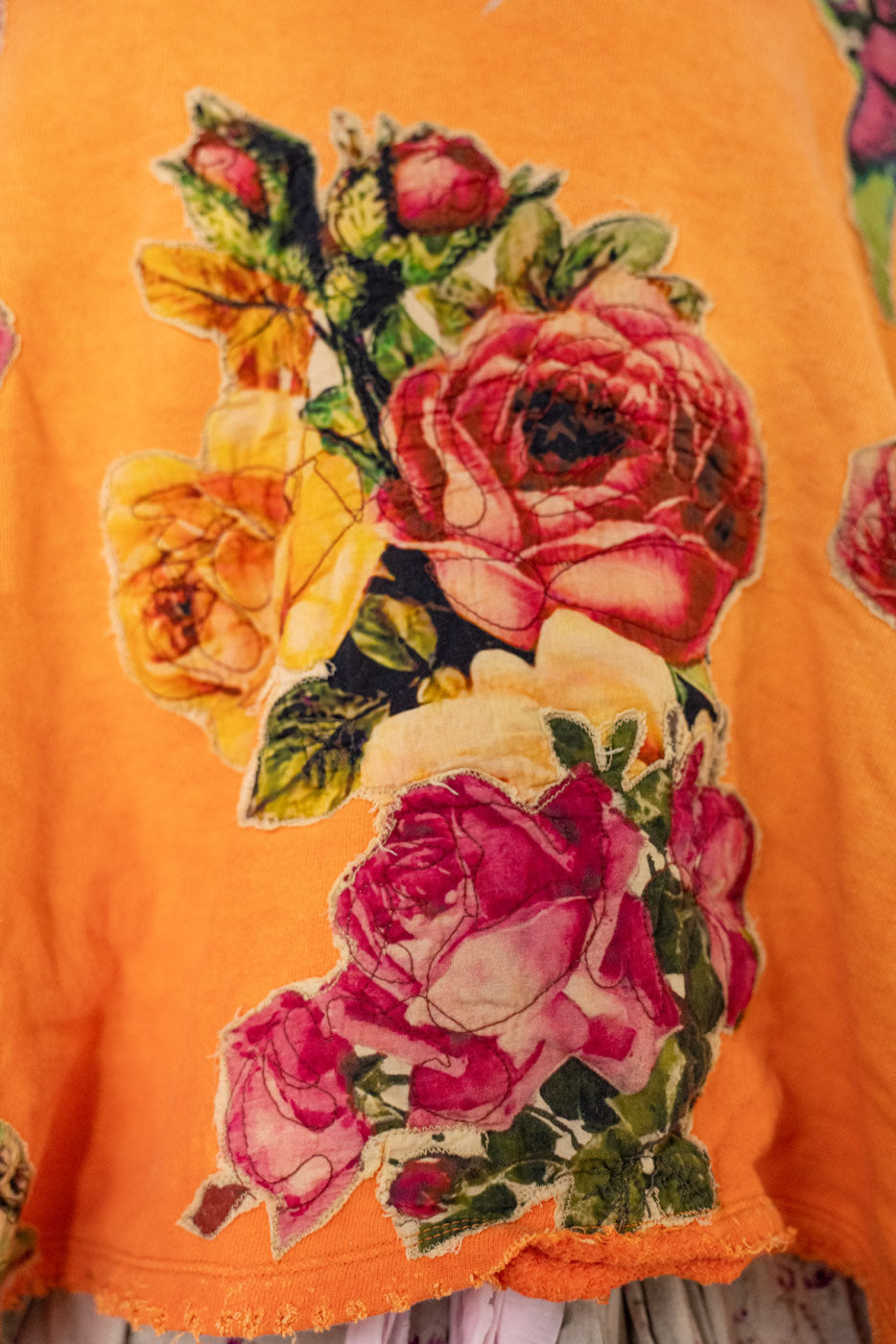 Close-up of a floral rose design on an orange sweatshirt.