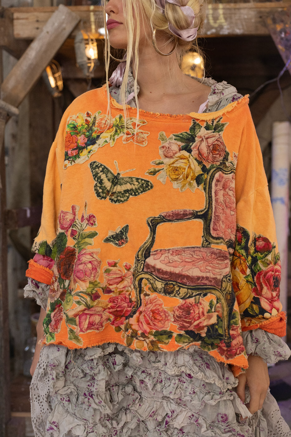Person wearing an orange floral and chair print sweatshirt with a blurred background