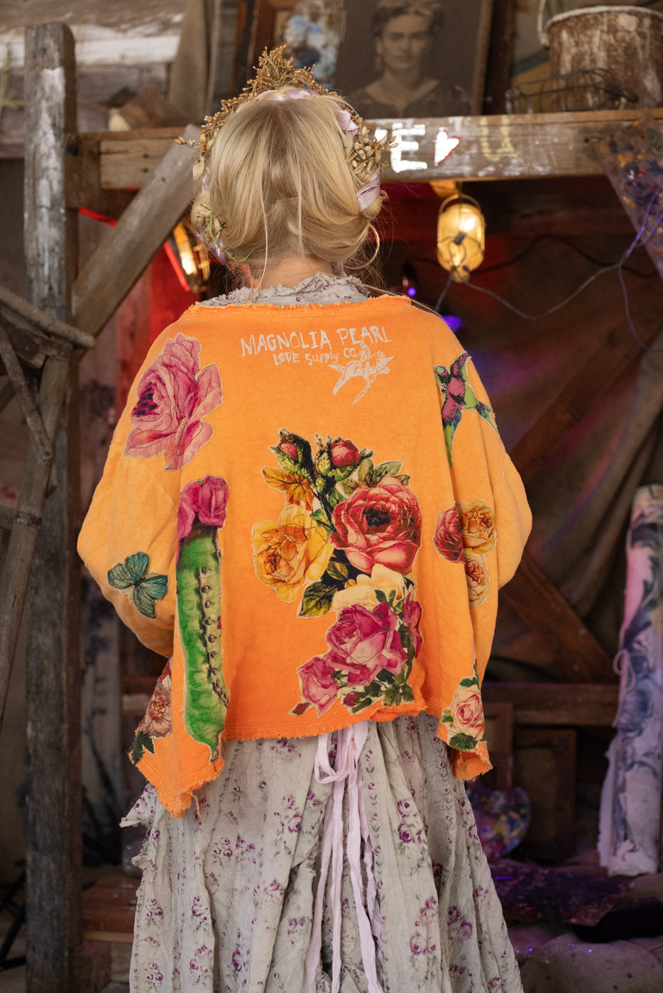 Person wearing a bright orange floral-patterned sweatshirt in a rustic setting.