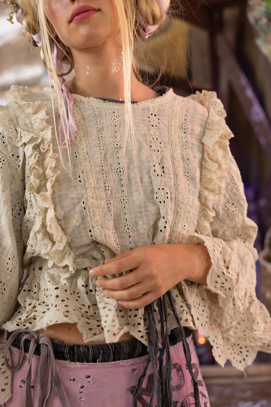 Person wearing a light-colored lace top with ruffled sleeves and patterned pants.