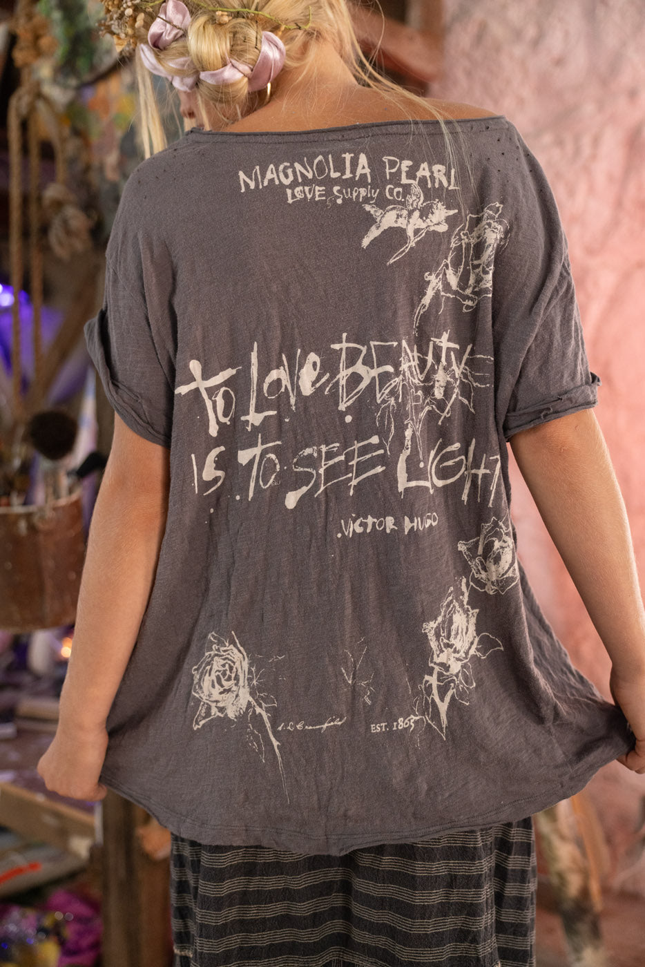 Person wearing a dark gray t-shirt with text and graphics, standing in a casual setting. "to love beauty is to see light" -Victor Hugo