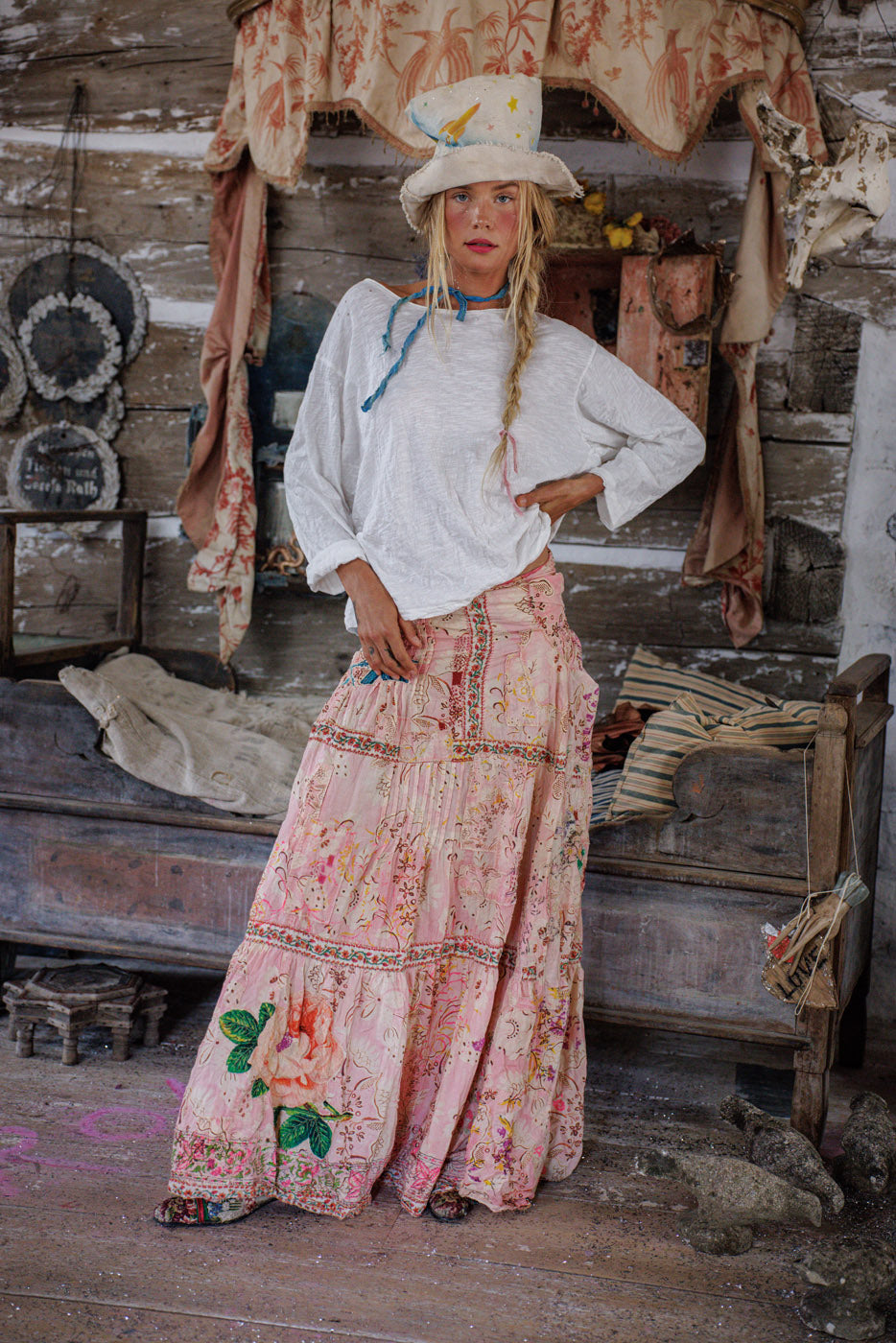 Woman in Magnolia Pearl artisan clothing, vintage style pink floral skirt, whimsical hat, rustic setting