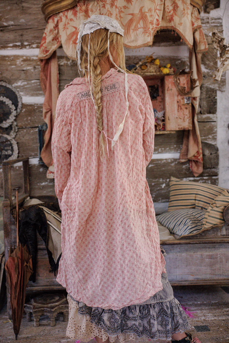 Woman in Magnolia Pearl pink artisan vintage dress with lace bonnet, rustic boho setting
